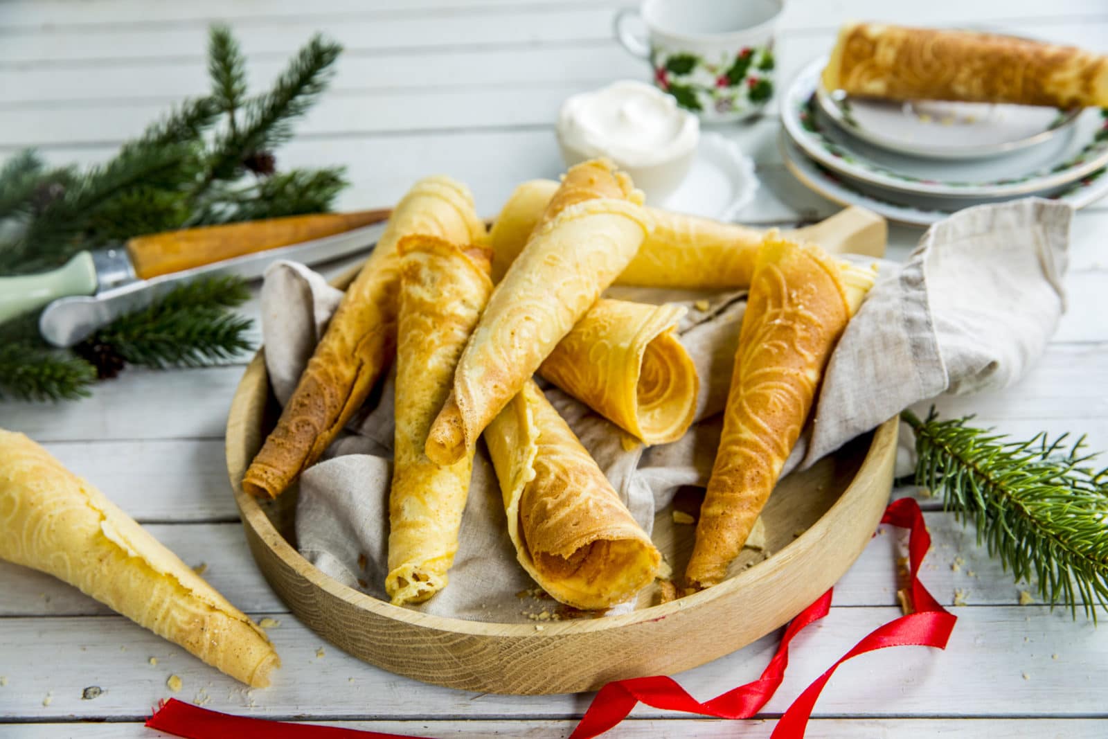 Glutenfrie krumkaker på trefat med grankvist i bakgrunnen