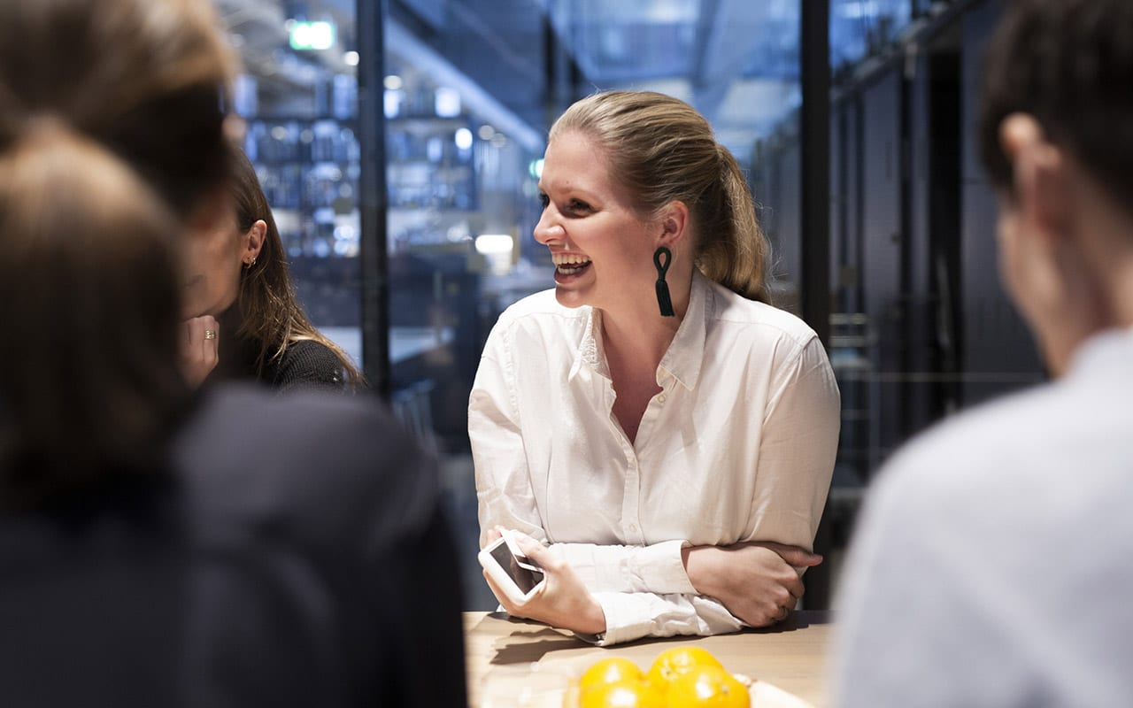 Kontoransatt smiler til kolleger. Foto.